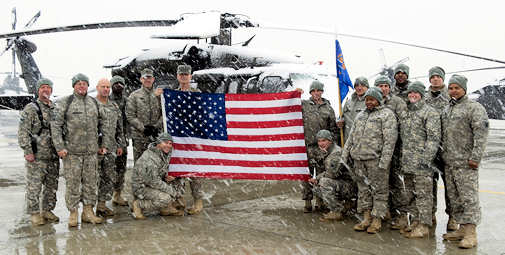 Members of A Company, 1-69 Aviation Regiment, hold the flag from Ground Zero, as snow falls at Bagram Air Base, Afghanistan, March 2, 2011. The 1-69 fly Blackhawk helicopters on various missions, from escorting VIPs to transporting detainees. Photo by British Sgt. Chris Hargreaves